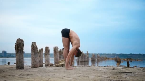 Hombre atleta practicando yoga en la orilla del río después del atardecer — Vídeo de stock