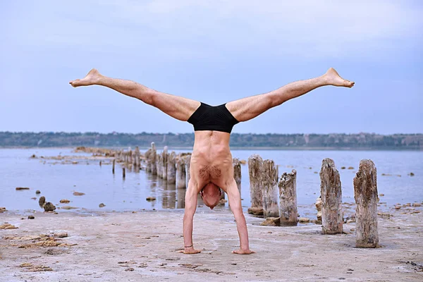 yoga man standing on hands and does the splits on pristine beach