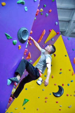 Climber on artificial climbing wall in bouldering gym without insurance. Extreme and healthy lifestyle concept. clipart