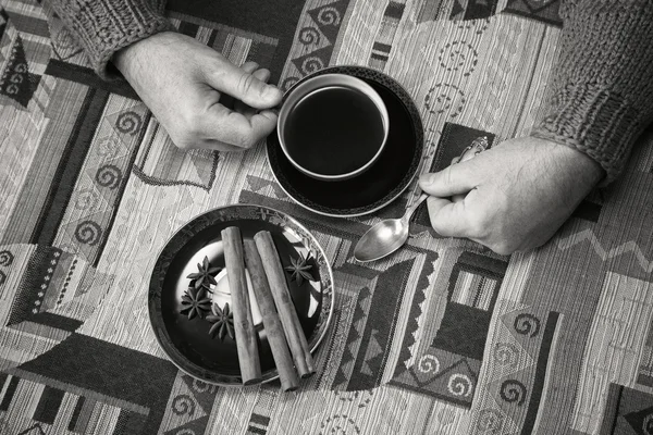 Manos masculinas sosteniendo una taza de café negro, especias en el plato palitos de canela y anís estrellado, vista superior . —  Fotos de Stock