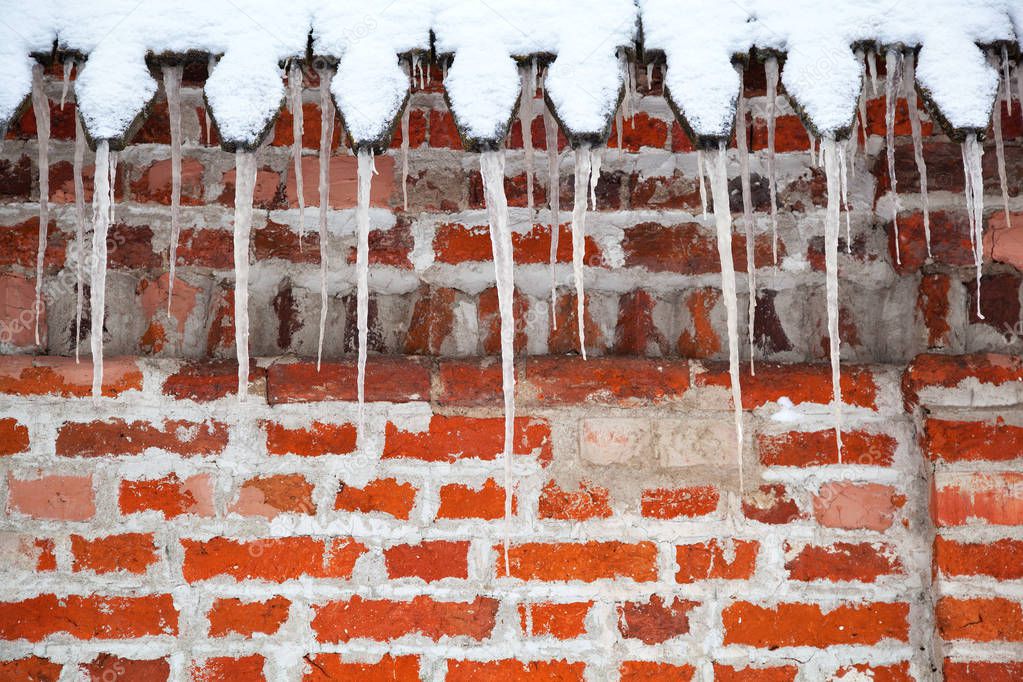 Icicles hang from the roof against a brick wall. Winter time