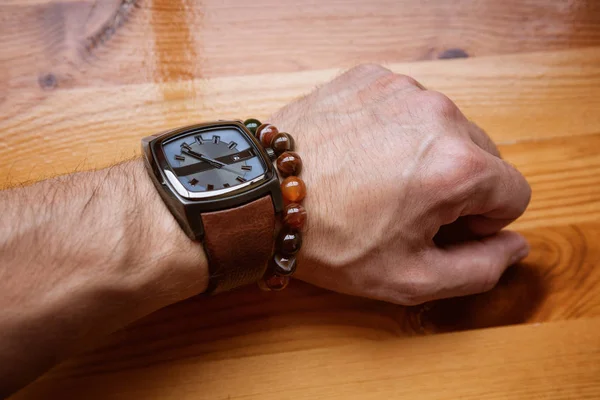 Tangan manusia dengan jam tangan dan gelang dekorasi di meja kayu latar — Stok Foto