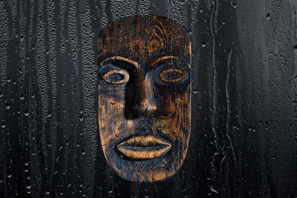 Máscara de madera marrón sobre fondo negro, a través de una gota de agua —  Fotos de Stock