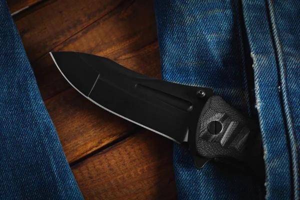 Black folding knife in his pocket on wooden background