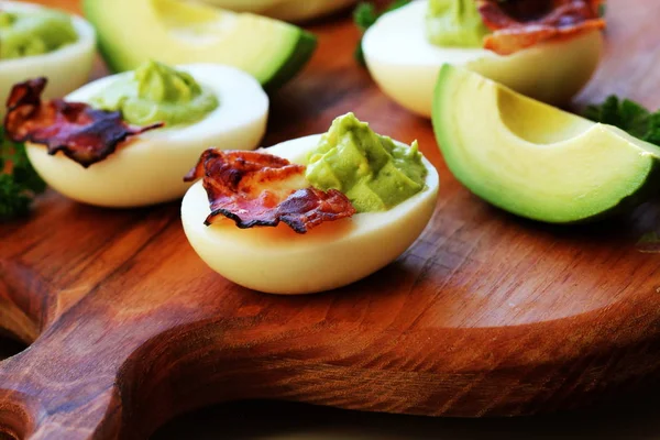 Фаршированные яйца с авокадо и беконом на доске — стоковое фото