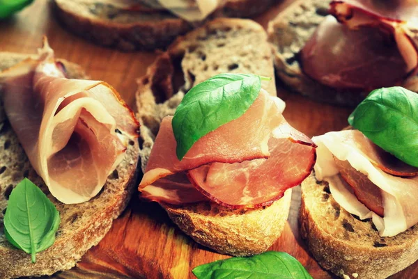 Italian ham prosciutto . Ingredients for bruschetta crostini. Rustic  view of sandwich. Ham with basil. — Stock Photo, Image