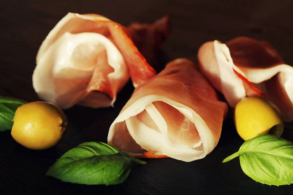 Curled Slices of Delicious Prosciutto with basil leaves and olives — Stock Photo, Image