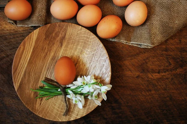 Påsk bakgrund. Rustika träbord med plattan, ägg, blommor och skärbräda. Ovanifrån. — Stockfoto