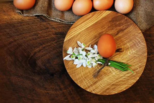 Pasen achtergrond. Rustieke houten tafel met plaat, ei, bloemen en snijplank. Bovenaanzicht. — Stockfoto