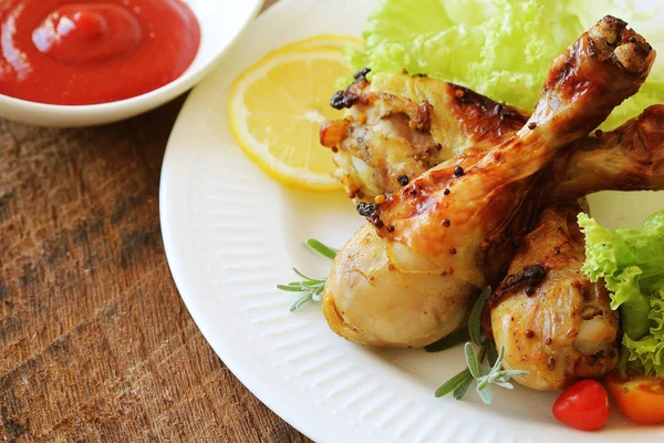 Grilled chicken legs with mustard on wooden table served on white plate with rosemary. BBQ dinner background — Stock Photo, Image