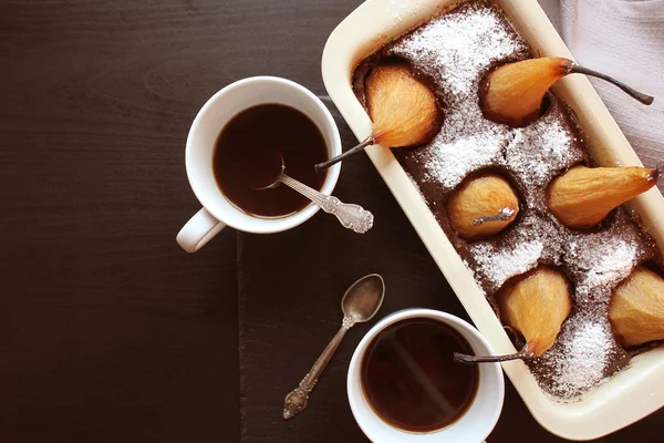 Torta al cioccolato con pere intere al forno all'interno e due tazze di caffè su sfondo scuro. Vista dall'alto — Foto Stock