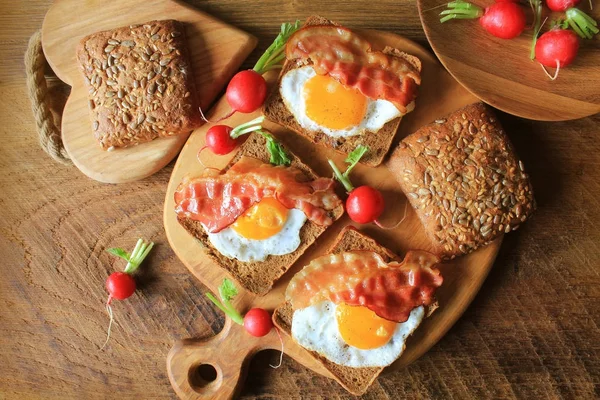 Сніданок, хрусткий бекон, смажені яйця та хліб. Бутерброди на обробній дошці. Русичний стіл. Вид зверху — стокове фото