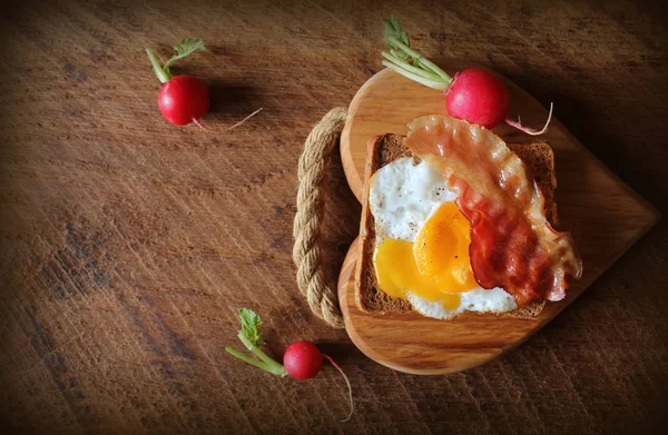 Сніданок, хрусткий бекон, смажені яйця та хліб. Сендвіч на обробній дошці. Русичний стіл. Вид зверху — стокове фото
