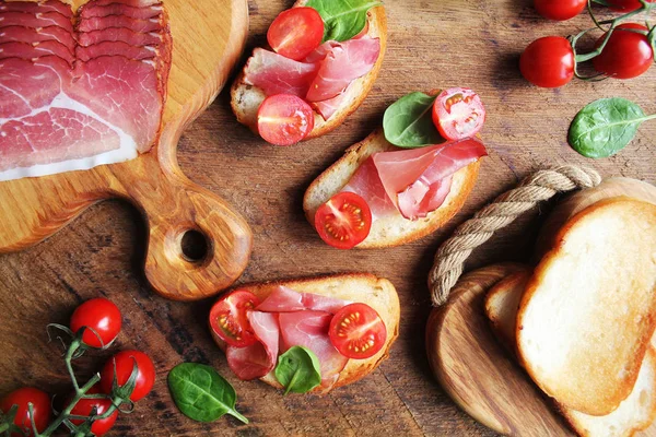 Bruschetta with prosciutto ham, cherry tomatoes and green spinach . Top view — Stock Photo, Image