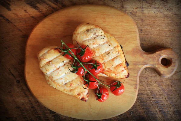 Peito de frango grelhado com tomates cereja, espinafre em uma tábua de madeira. Vista superior — Fotografia de Stock