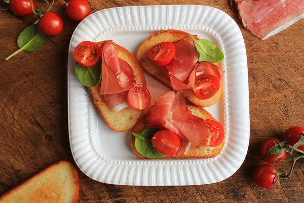 Bruschetta with prosciutto ham, cherry tomatoes and green spinach . Top view — Stock Photo, Image