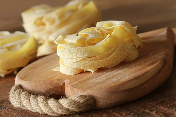 Nid de tagliatelles de pâtes sur planche à découper en bois aon fond rustique. Concentration sélective — Photo