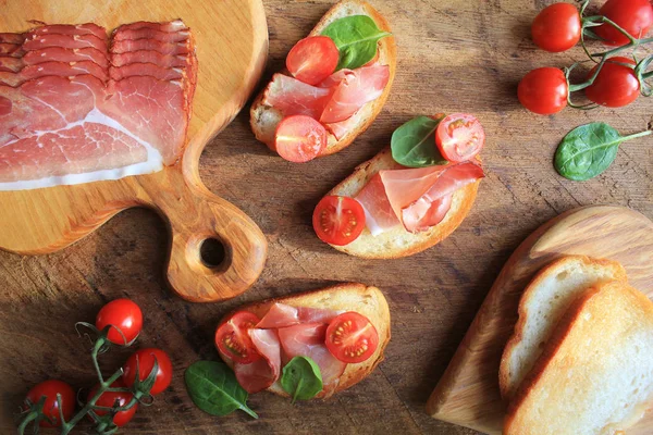 Bruschetta with prosciutto ham, cherry tomatoes and green spinach . Top view — Stock Photo, Image