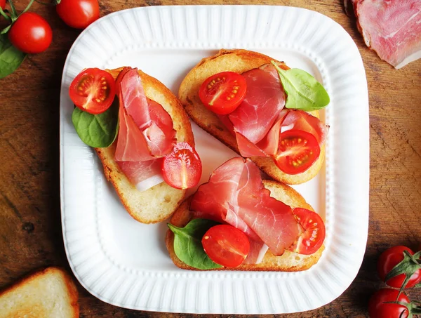 Bruschetta with prosciutto ham, cherry tomatoes and green spinach . Top view — Stock Photo, Image