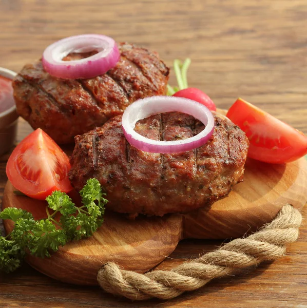 Homemade burger with beef cutlet, vegetables, onion and herbs on wooden cutting board — Stock Photo, Image