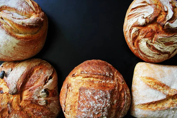 Brood. Assortiment van verschillende soorten brood op een zwarte achtergrond. Brood, broodjes, stokbrood, cornflakes. Bakkerijproducten. — Stockfoto