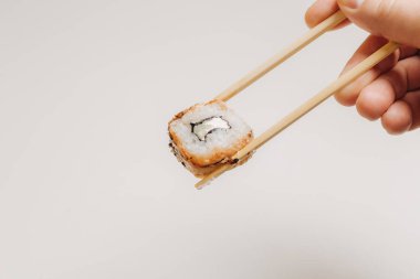 El ele tutuşan suşi beyaz arka planda iki çubuk yuvarlar.