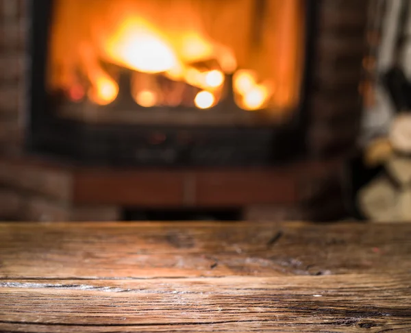 Mesa de madeira velha e lareira com fogo quente no fundo . — Fotografia de Stock