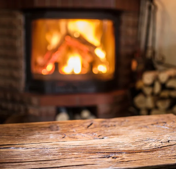 Old wooden table and fireplace with warm fire on the background. — Stock Photo, Image