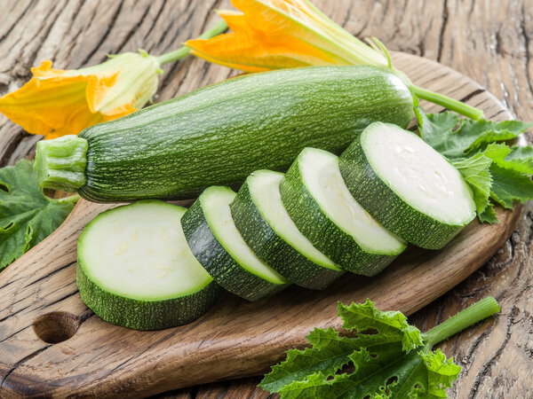 Zucchini with slices and zucchini flowers on a wooden table.