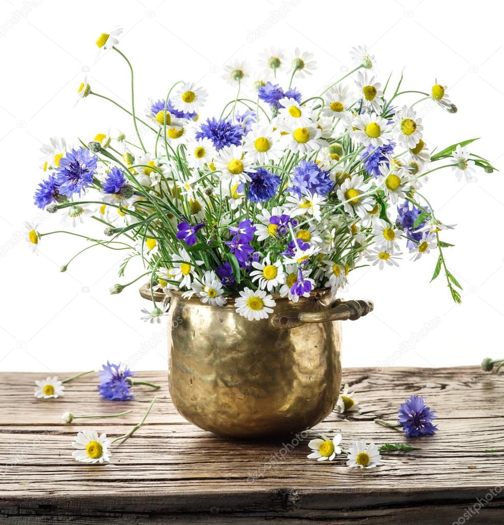 Bouquet of chamomiles and corn flowers in the vase on the wooden