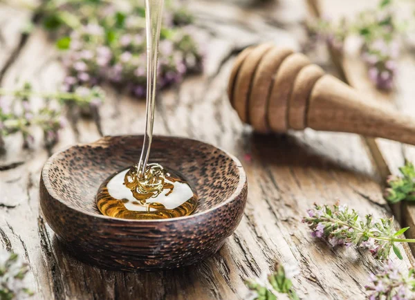 Miele alle erbe versato nella ciotola di legno. Ciotola è su legno vecchio Foto Stock