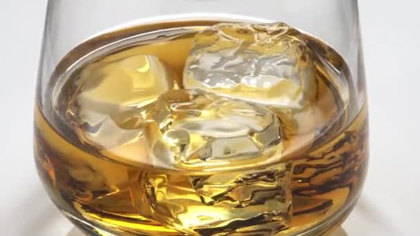 Whisky gegoten in een glas met ijs. Glas wordt gedraaid. 4k video. — Stockvideo