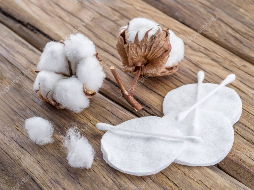 Fluffy cotton ball and cotton swabs and pads on wooden table.