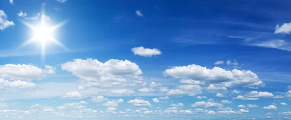 Weiße Haufenwolken und strahlende Sonne am blauen Himmel. — Stockfoto