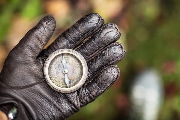 Man's hand in a leather glove holding a compass. Nature backgrou — Stock Photo, Image