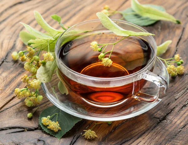Pohár z lipové čaje a limetkové květy na dřevěný stůl. — Stock fotografie
