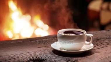 Kahve yanan bir şömine önünde eski bir ahşap tahta üzerinde duruyor. Buhar bir fincan kahve yükselir. 1920 x 1080 ilmekledi video