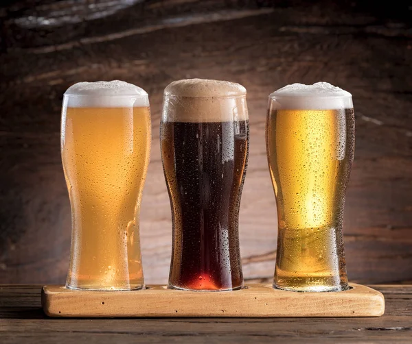 Três copos de cerveja na mesa de madeira . — Fotografia de Stock