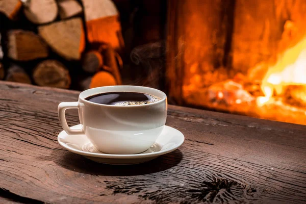 Tazza di caffè caldo sul tavolo di legno e camino sul retro — Foto Stock