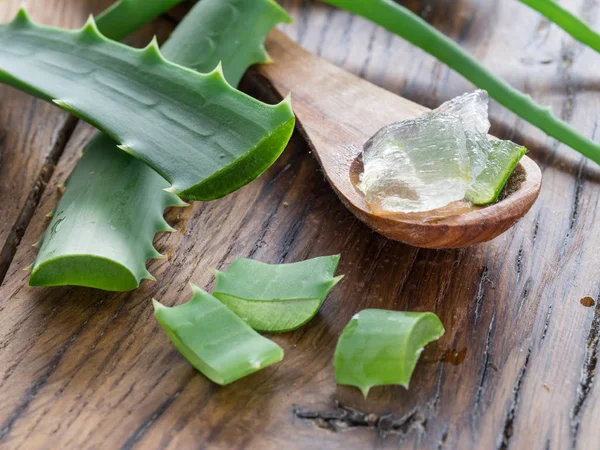 Hojas de aloe frescas y gel de aloe en la cuchara de madera sobre la mesa . — Foto de Stock