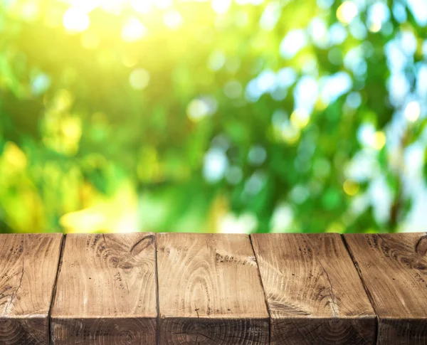 Alte hölzerne Tischplatte und grünes Laub im Hintergrund. — Stockfoto