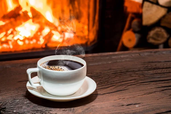 Чашка гарячої кави на дерев'яному столі і камін на задньому плані — стокове фото