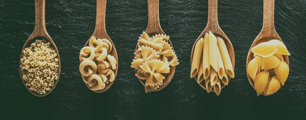 Verschillende pastasoorten in houten lepels op tafel. Bovenaanzicht. — Stockfoto