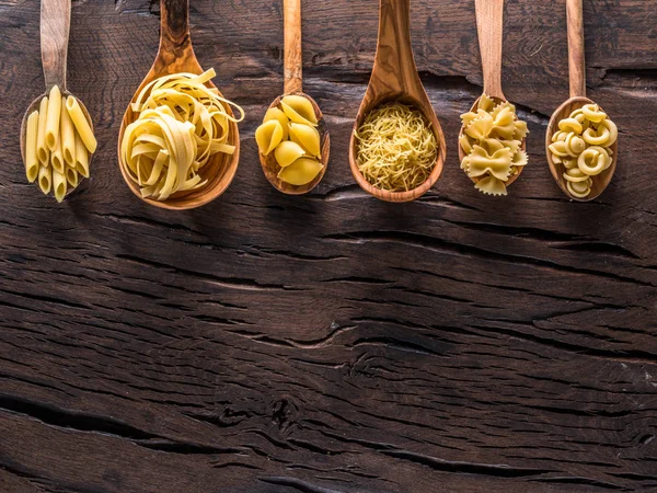 Diversi tipi di pasta in cucchiai di legno sul tavolo. Vista dall'alto. — Foto Stock