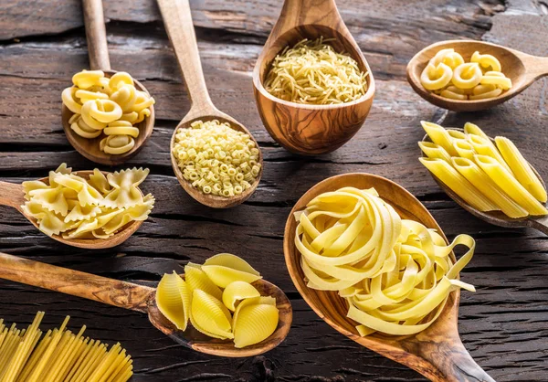 Verschillende pastasoorten in houten lepels op tafel. Bovenaanzicht. — Stockfoto