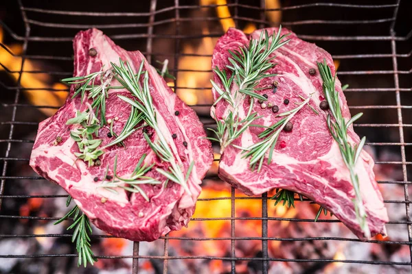 Rib Eye Steaks und Grill mit loderndem Feuer dahinter. — Stockfoto