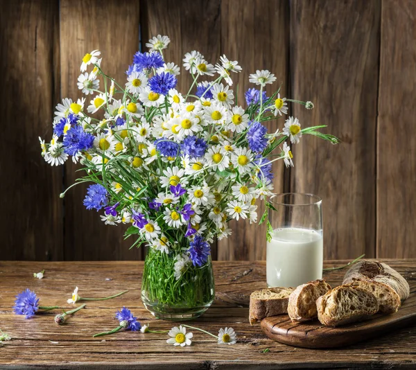 Bouquet di fiori di campo, bicchiere di latte e pane morbido sul wo — Foto Stock