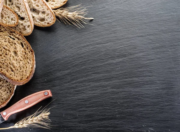 Bread slices, a wheat and a knife on the black stone desk. — Stock Photo, Image
