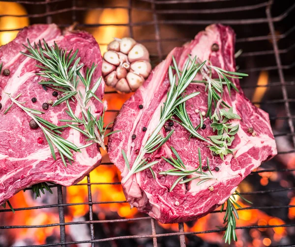 Filetes de costilla y parrilla con fuego ardiente detrás de ellos . —  Fotos de Stock