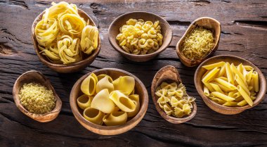 Different pasta types in wooden bowls on the table. Top view. clipart